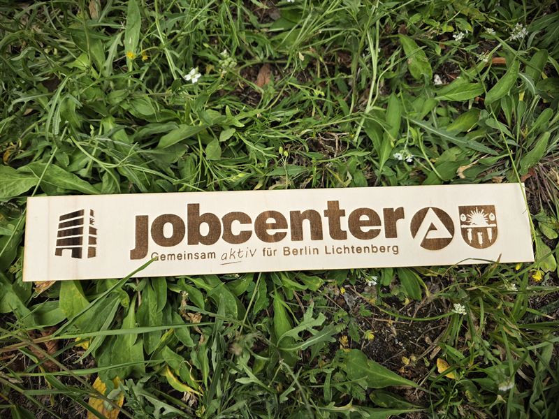 Gravierte Holzleiste mit Jobcenter-Logo im Gras